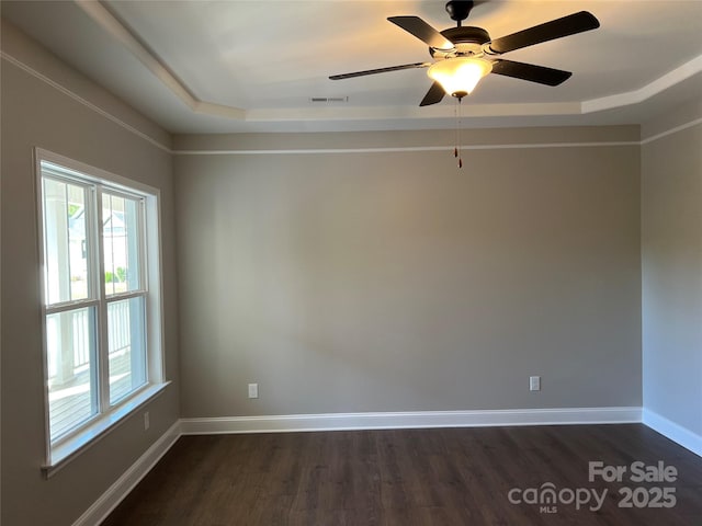 empty room with a raised ceiling, dark wood-type flooring, baseboards, and visible vents