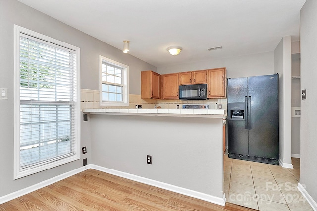 kitchen featuring backsplash, kitchen peninsula, black appliances, and light hardwood / wood-style floors