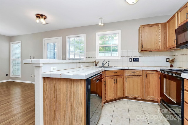 kitchen featuring tile countertops, backsplash, black appliances, light wood-type flooring, and kitchen peninsula