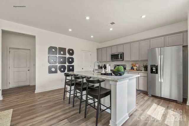 kitchen with a kitchen island with sink, stainless steel appliances, gray cabinets, a kitchen breakfast bar, and light hardwood / wood-style flooring