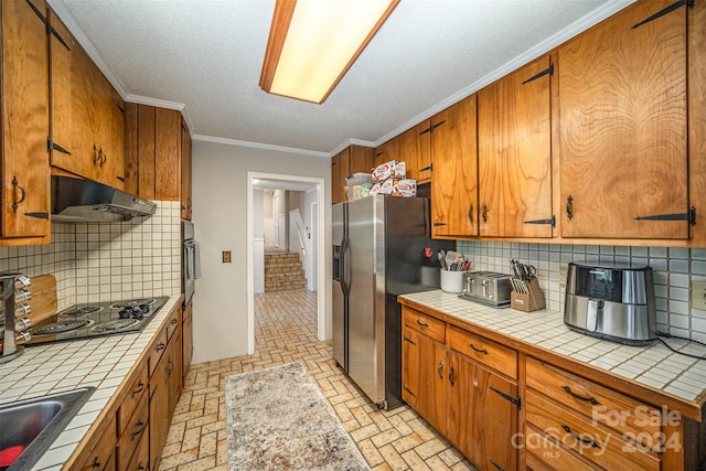 kitchen featuring tasteful backsplash, sink, stainless steel appliances, tile counters, and crown molding