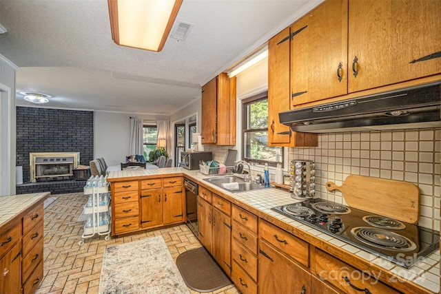 kitchen with decorative backsplash, tile counters, sink, electric cooktop, and a brick fireplace