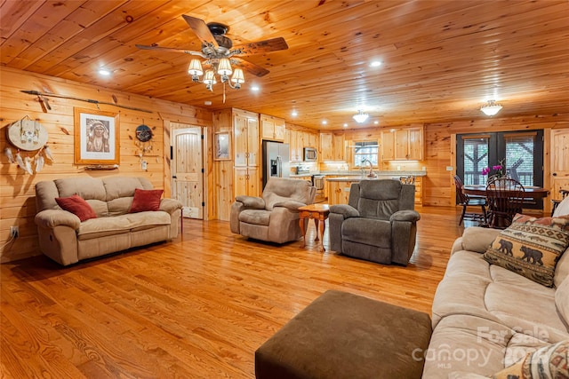 living room with ceiling fan, sink, light hardwood / wood-style flooring, wooden ceiling, and wood walls