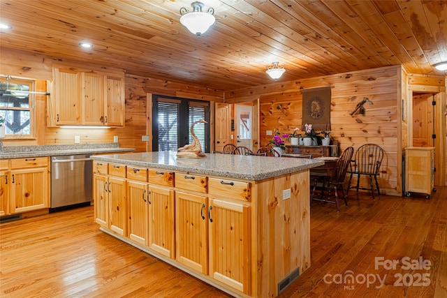 kitchen featuring dishwasher, a center island, light stone counters, and wood walls