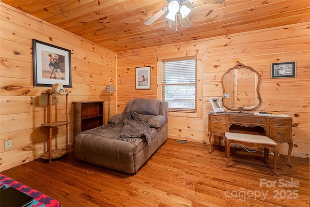 living area featuring wooden walls, light hardwood / wood-style flooring, ceiling fan, and wooden ceiling