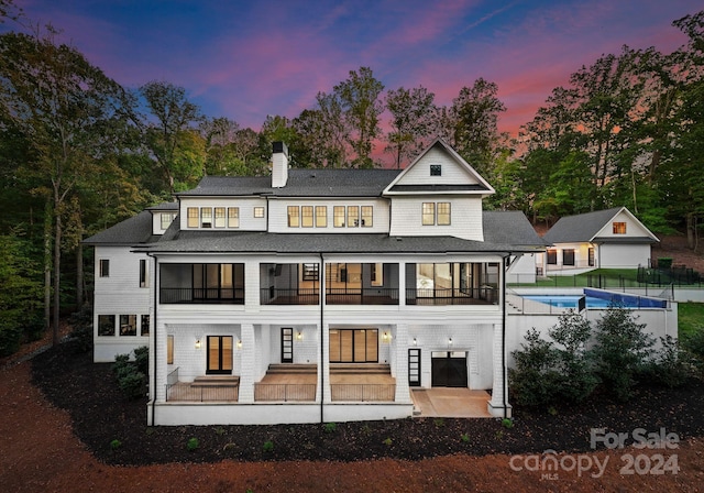 back house at dusk with a patio, an outbuilding, and a balcony