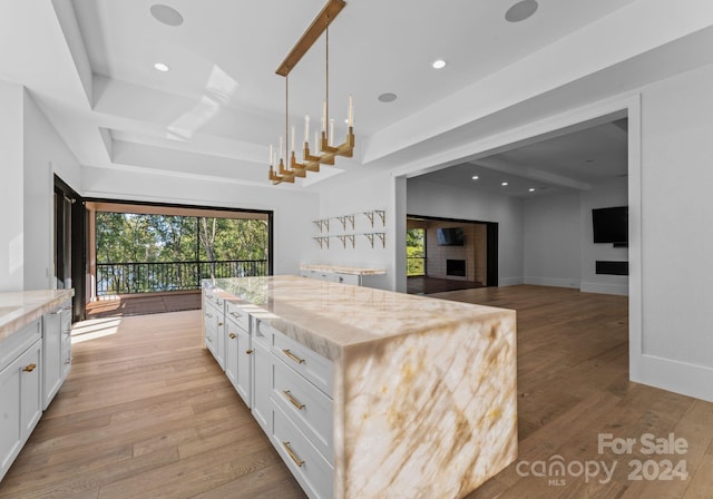 kitchen with light hardwood / wood-style flooring, light stone countertops, decorative light fixtures, and white cabinets