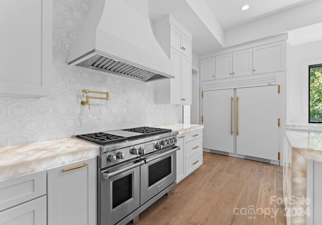 kitchen with high end appliances, custom exhaust hood, white cabinets, and light wood-type flooring