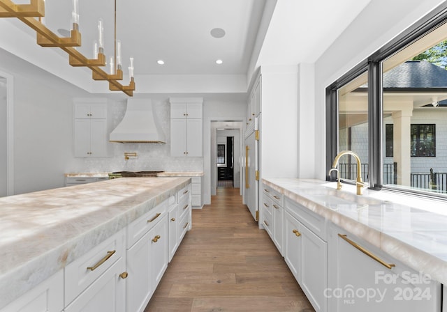 kitchen with light stone countertops, white cabinets, and custom range hood