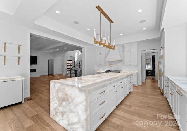 kitchen with a spacious island, custom exhaust hood, white cabinets, and light hardwood / wood-style flooring