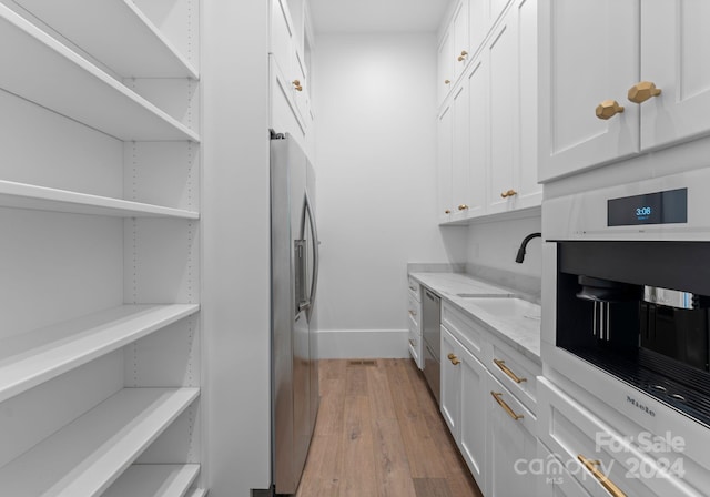 kitchen with sink, light stone countertops, white cabinetry, light wood-type flooring, and appliances with stainless steel finishes