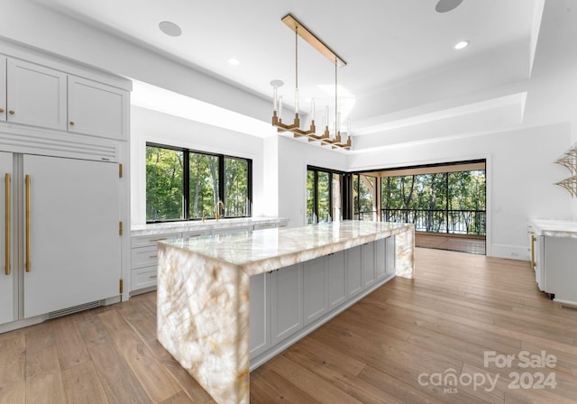 kitchen with white cabinets, a healthy amount of sunlight, light stone countertops, and paneled fridge