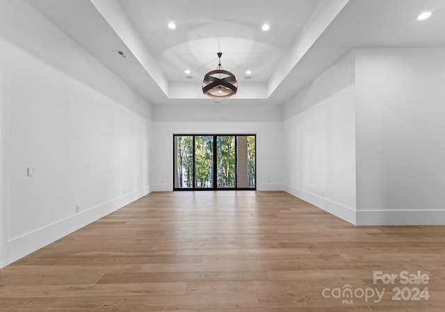 empty room featuring light hardwood / wood-style flooring, a chandelier, and a tray ceiling