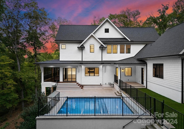 back house at dusk with a patio area and a fenced in pool