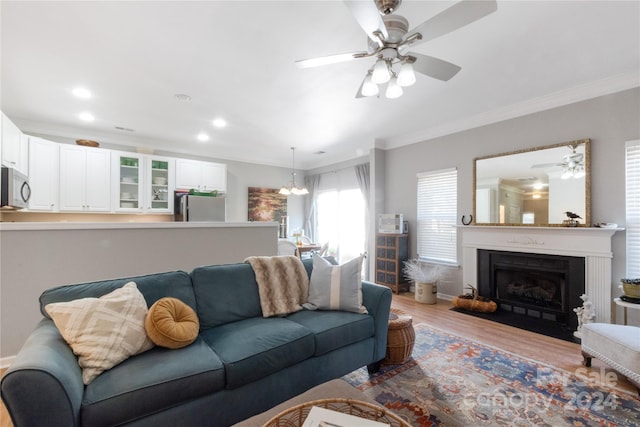 living room with light hardwood / wood-style flooring, ceiling fan with notable chandelier, and crown molding