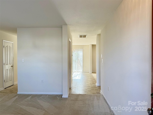 hall with light carpet, baseboards, and visible vents