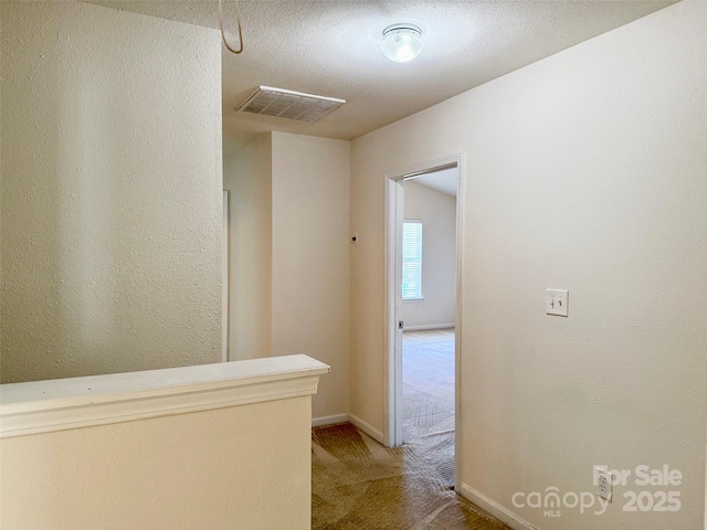 hallway with light colored carpet, visible vents, a textured ceiling, and baseboards