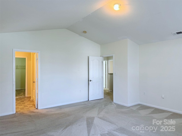 unfurnished bedroom featuring baseboards, visible vents, light colored carpet, lofted ceiling, and a walk in closet