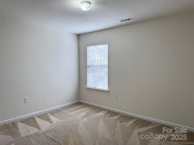 spare room featuring carpet floors, visible vents, and baseboards