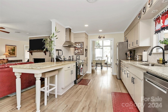 kitchen with appliances with stainless steel finishes, sink, light wood-type flooring, wall chimney exhaust hood, and decorative backsplash