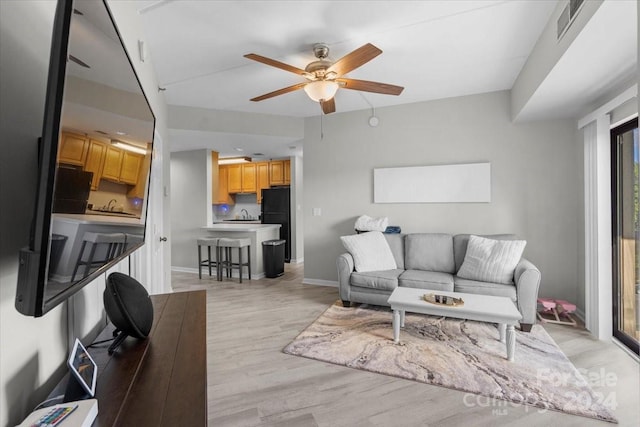 living room featuring sink, light wood-type flooring, and ceiling fan