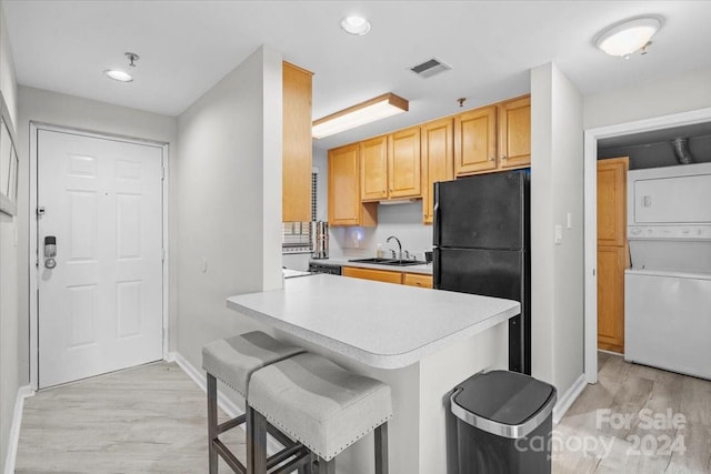 kitchen featuring stacked washer and clothes dryer, a breakfast bar area, black refrigerator, kitchen peninsula, and light hardwood / wood-style floors