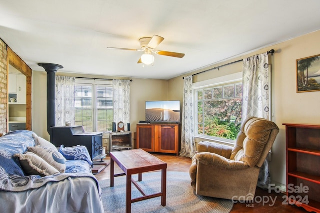 living room with wood-type flooring, a wood stove, and ceiling fan