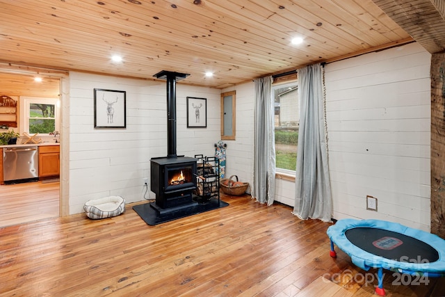 living room featuring wooden walls, a wood stove, wooden ceiling, electric panel, and light hardwood / wood-style flooring