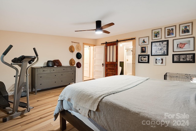 bedroom with light wood-type flooring, ceiling fan, and a barn door