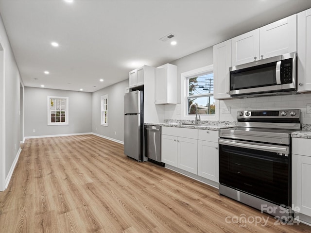 kitchen with appliances with stainless steel finishes, white cabinetry, and light hardwood / wood-style floors