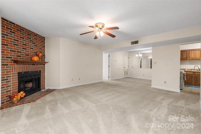 unfurnished living room with sink, light carpet, a fireplace, and ceiling fan with notable chandelier