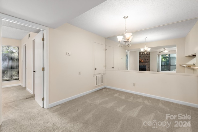 spare room with light carpet, a textured ceiling, ceiling fan with notable chandelier, and a fireplace