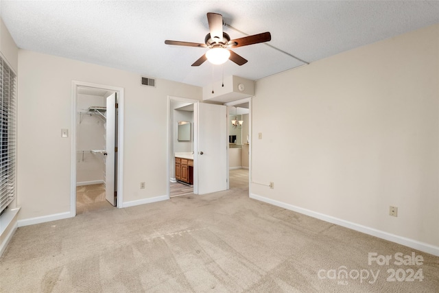 unfurnished bedroom featuring light carpet, ceiling fan, a closet, a walk in closet, and ensuite bath