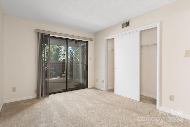 unfurnished bedroom featuring a closet, light carpet, a textured ceiling, and access to exterior