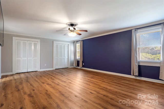 unfurnished bedroom featuring ornamental molding, hardwood / wood-style flooring, ceiling fan, and multiple closets