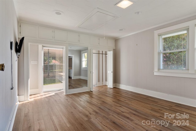 unfurnished room featuring ornamental molding, wooden walls, a wealth of natural light, and light hardwood / wood-style floors