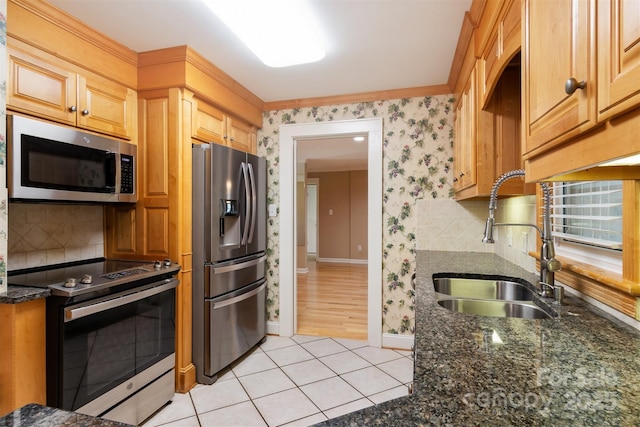 kitchen with wallpapered walls, light tile patterned floors, dark stone counters, appliances with stainless steel finishes, and a sink