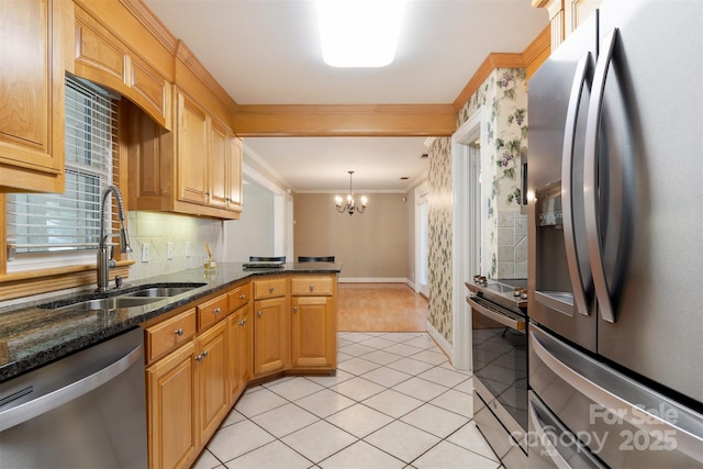 kitchen with a sink, ornamental molding, appliances with stainless steel finishes, dark stone counters, and pendant lighting