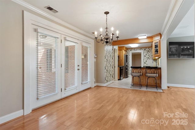 unfurnished dining area with crown molding, light wood finished floors, visible vents, baseboards, and wallpapered walls