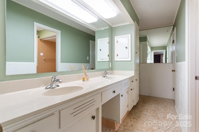 full bath featuring double vanity, a wainscoted wall, tile walls, and a sink