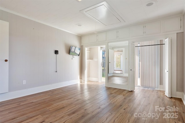 unfurnished room with baseboards, light wood-type flooring, attic access, and crown molding