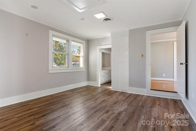 unfurnished bedroom with crown molding, visible vents, attic access, wood finished floors, and baseboards