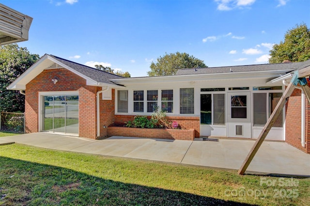 rear view of house featuring a yard, brick siding, roof with shingles, and a patio area