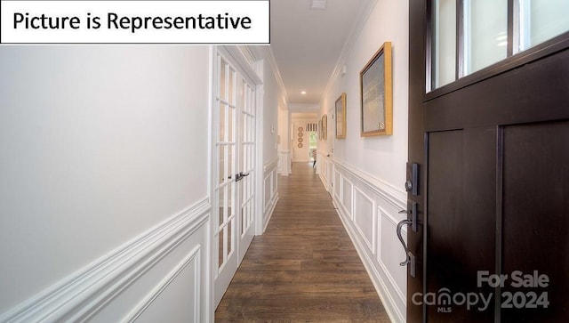 corridor featuring crown molding, a decorative wall, wainscoting, and dark wood-style flooring