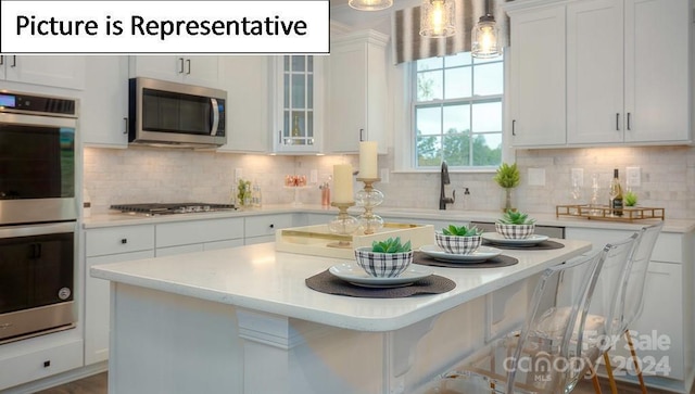 kitchen with light countertops, backsplash, a kitchen island, white cabinets, and appliances with stainless steel finishes