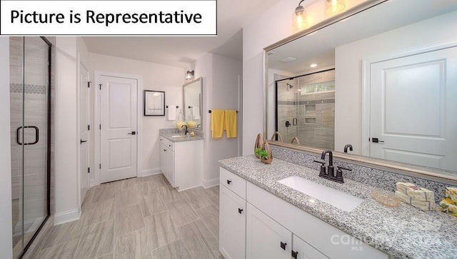 bathroom featuring two vanities, baseboards, a sink, and a stall shower