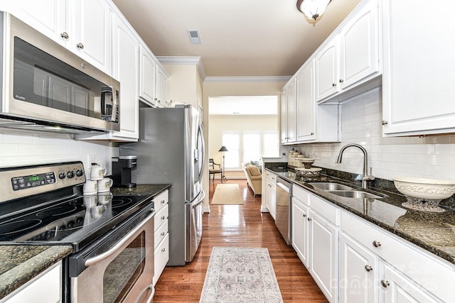 kitchen featuring appliances with stainless steel finishes, white cabinetry, dark stone countertops, and sink