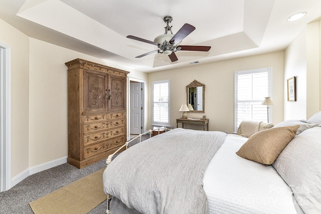 carpeted bedroom featuring ceiling fan, multiple windows, and a tray ceiling