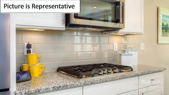 kitchen with tasteful backsplash, white cabinets, light stone countertops, and stainless steel appliances
