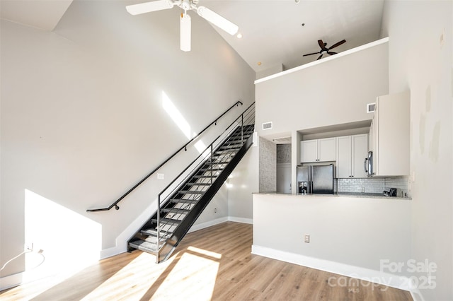 stairs with hardwood / wood-style flooring, high vaulted ceiling, and ceiling fan